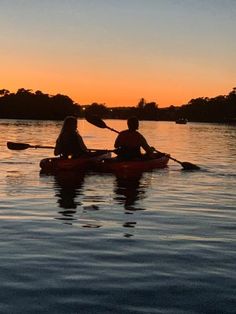 two people are kayaking in the water at sunset