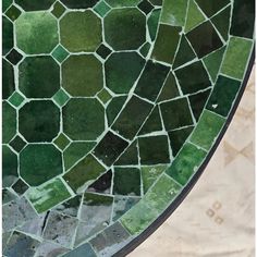 a close up view of a green and black mosaic tile design on the side of a table