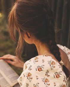 a woman reading a book while wearing a flowered top and braid in her hair