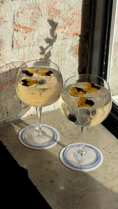 two glasses filled with drinks sitting on top of a window sill next to a brick wall