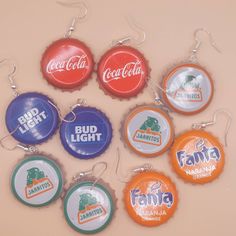 six soda bottle caps are hanging from silver earwires on a pink background with the words, bud light, fanta, and coca - cola