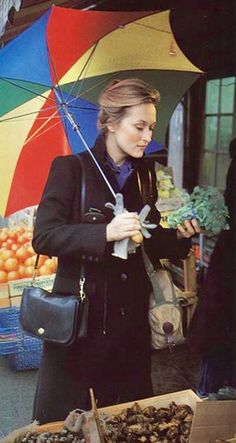 a woman standing under an umbrella next to fruit and vegetables