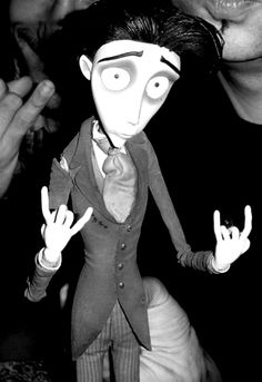 a black and white photo of a doll with two fingers up in the air next to a man's face