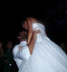 a bride and groom hugging each other in front of a group of people at night