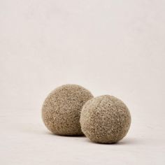 two wool balls sitting next to each other on a white surface with one ball in the middle