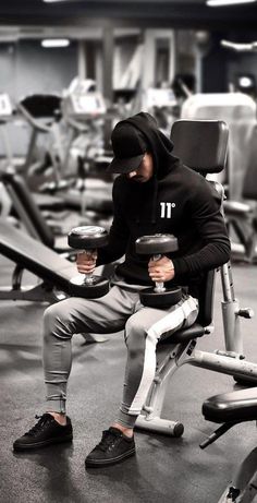 a man sitting on top of a bench holding two dumbbells in a gym