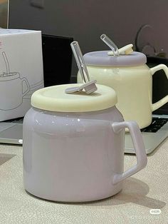 a laptop computer sitting on top of a table next to two mugs with spoons in them