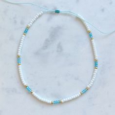 White seed bead choker necklace with an aqua/turquoise blue pattern and gold accents. Necklace length is adjustable by tightening or loosening sliding knot closure. necklace length is 13 inches fully tightened or 26 inches when fully extended. This necklace is waterproof and perfect for a day at the beach or the pool! Preppy Seed Bead Necklace, Blue Seed Bead Bracelet, Bead Necklace Ideas Vsco, Summer Necklace Ideas, Seed Bead Necklace Ideas, Seed Bead Necklace Patterns, Blue And Gold Jewelry, Beachy Necklaces, Beachy Necklace