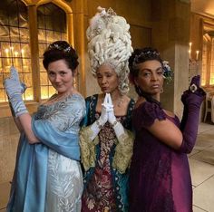 three women dressed in fancy clothing posing for the camera with one holding up her hand