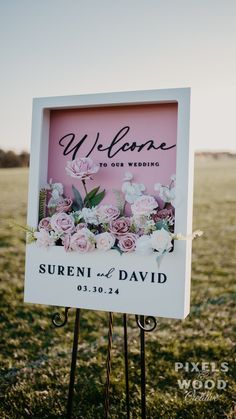 a welcome sign in the grass with flowers on it and a pink background that says welcome to our wedding