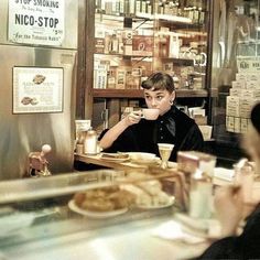 a woman sitting at a table in front of a counter with food and drinks on it