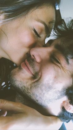 a man and woman kissing each other while laying on top of a bed with their eyes closed