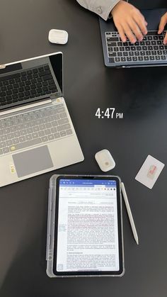 two laptops sitting on top of a table next to an open book and pen