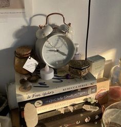 a stack of books with an alarm clock sitting on top of it next to other items