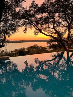 an empty swimming pool with the sun setting in the background and trees reflecting on the water