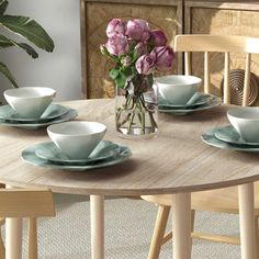 a wooden table topped with white plates and bowls next to a vase filled with pink flowers