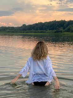 a woman is sitting in the water with her hands on her knees and looking at the sky