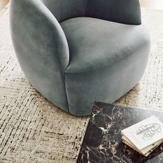 a gray chair sitting on top of a rug next to a table with a book