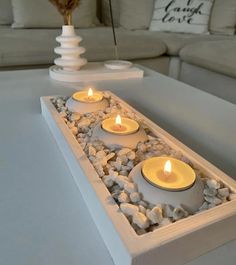 three lit candles are placed in a decorative tray with rocks and pebbles on the bottom