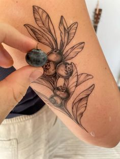 a woman with a tattoo on her arm holding up a piece of fruit and leaves