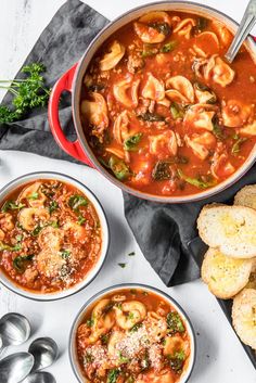 two bowls of pasta soup with bread on the side and spoons next to it