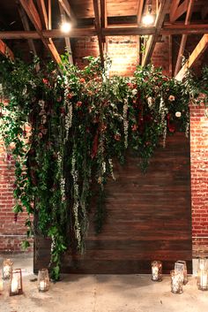 candles and greenery are arranged on the wall in this rustic wedding ceremony space with wood paneling