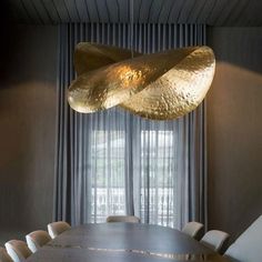 a dining room table with chairs and a large gold sculpture hanging from the ceiling