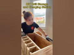 a woman in black shirt and gloves working on a wooden box with windows behind her