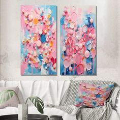 two paintings are hanging on the wall in a living room with white furniture and pillows