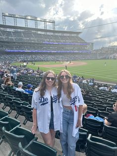 two young women standing in the stands at a baseball game wearing dodgers shirts and jeans