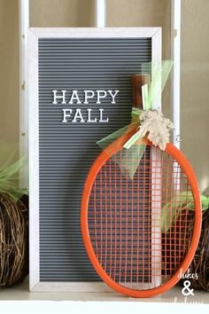 a happy fall sign with an orange racquet in front of it on a shelf