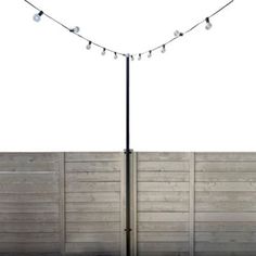 a pole with some lights on it next to a fence and grass area in front of a white wall