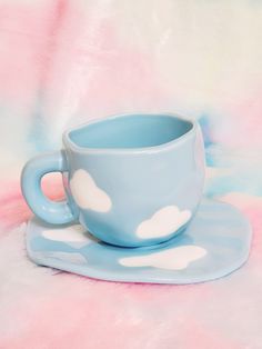 a blue cup and saucer sitting on top of a pink tablecloth with clouds