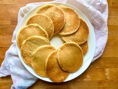 pancakes on a white plate sitting on top of a wooden table next to a napkin