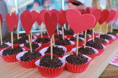 cupcakes with chocolate frosting and hearts on sticks in red paper wrappers