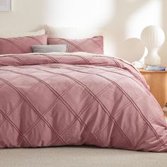 a bed with pink comforter and pillows in a bedroom area next to a night stand