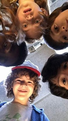 four children standing in a circle with their heads tilted to the side and looking up at the camera