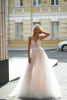 a woman in a wedding dress standing on the street with her hands behind her head