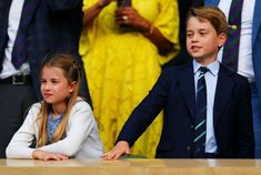 two young children sitting at a table in front of other people wearing suits and ties