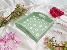 a green box sitting on top of a white sheet next to flowers and paintbrushes