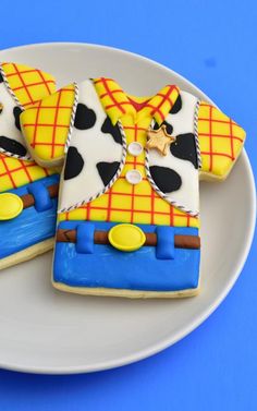 two decorated cookies on a white plate with blue and yellow designs, one is wearing a plaid shirt