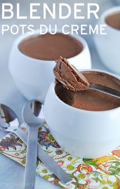 two white bowls filled with chocolate pudding on top of a table next to spoons