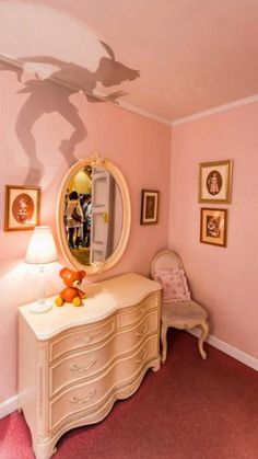 a room with pink walls and pictures on the wall, including a dresser and mirror