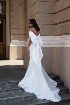 a woman in a white wedding dress standing on steps with her back to the camera