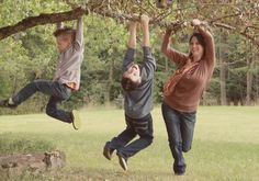 three people jumping up in the air with their arms and legs above them, while one person is holding onto a tree branch