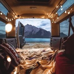 the inside of an rv with lights and blankets on the bed in front of it