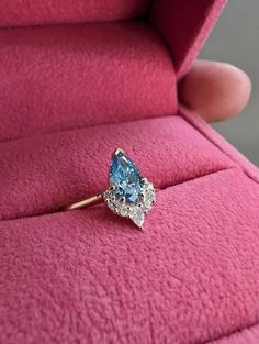 a blue diamond ring sitting on top of a pink velvet cushion