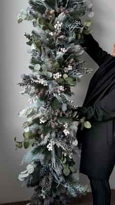 a woman is standing next to a christmas tree that has been decorated with greenery and pine cones