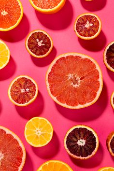 oranges and grapefruit cut in half on a pink background