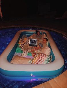 two people laying in an inflatable pool with a laptop